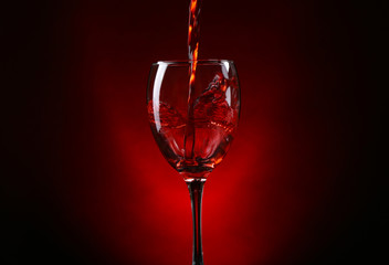 Wine pouring in glass on dark red background