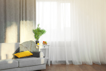 Grey sofa and small table with green plant on curtain background