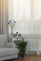 Grey sofa, small table and green plants on curtain background