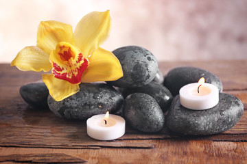 Fototapeta na wymiar Spa still life with stones, flower and candlelight on blurred pastel background