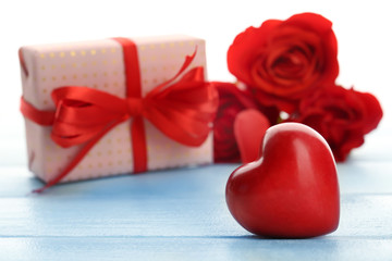 Gift box, rose flowers and decorative hearts on color wooden table, on light background
