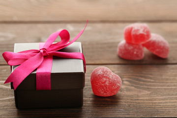 Gift box and jelly hearts on wooden background