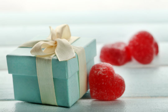 Gift box and  jelly hearts on color wooden background