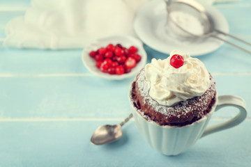 Mug cake with cream and cranberry on blue wooden background
