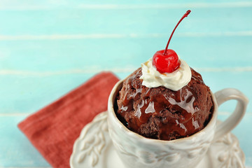 Chocolate mug cake with cream and cherry on blue wooden background