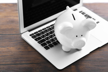Piggy bank with laptop on wooden table indoors