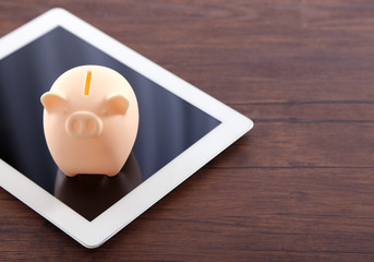 Piggy bank with tablet on wooden background