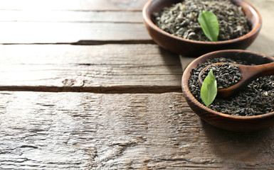 Dry tea in two bowls with green leaves on wooden table background