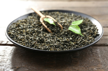 Dry tea with green leaves in black plate on wooden table background