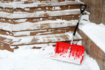 Red shovel for snow removal beside stairs