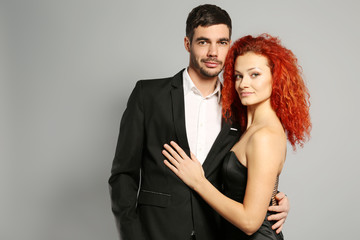 Happy young couple in black dress and suit embracing on grey background