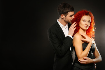 Young couple in dress and suit embracing on black background