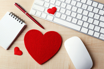 Computer peripherals with red hearts, pen and notebook on light wooden table