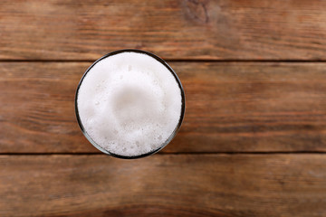 Glass of light beer with froth on wooden background