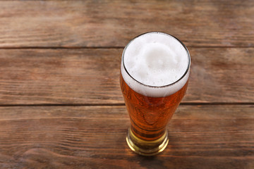 Glass of light beer with froth on wooden background