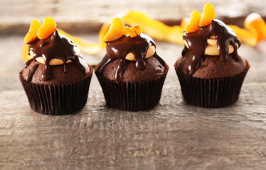 Three tasty cupcakes with slice of mandarin and chocolate on wooden background