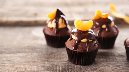 Three tasty cupcakes with slice of mandarin and chocolate on wooden background