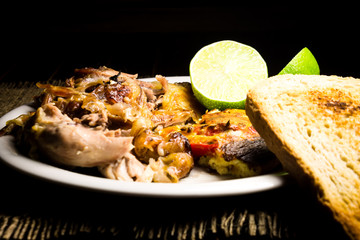 Roasted pork meat, limes and scrambled eggs with red papers and slices of bread 