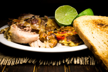 Roasted pork meat, limes and scrambled eggs with red papers and slices of bread 