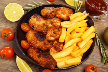 Baked chicken wings with French fries on wooden table