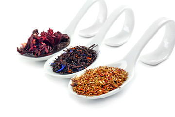 Different sorts of dry tea in ceramic spoons, isolated on white