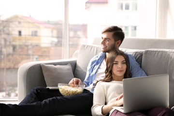 Young man watching TV and woman using laptop on a sofa at home