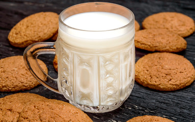 Cup of milk with oatmeal cookies on the black wooden background