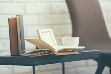 Open book with cup on black small table against white brick wall, close up