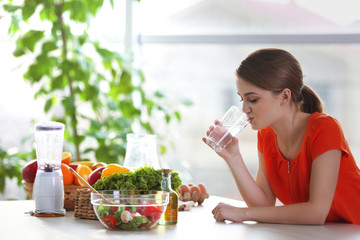 Young woman drinking water near table with fruits and vegetables in the kitchen