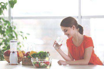 Young woman drinking water near table with fruits and vegetables in the kitchen