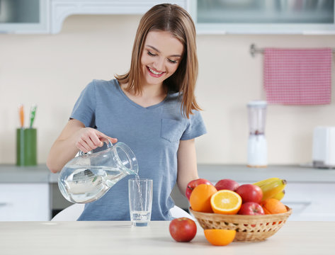 Young woman pouring water from jug into glass in the kitchen