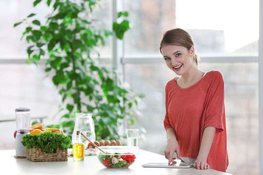 Young woman with tablet at table with fruits and vegetables in the kitchen