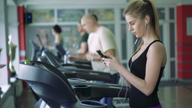 Beautiful blonde on the treadmill uses the phone and listening to music. 4k