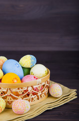 Colorful Easter eggs in wicker basket on textile on dark wooden