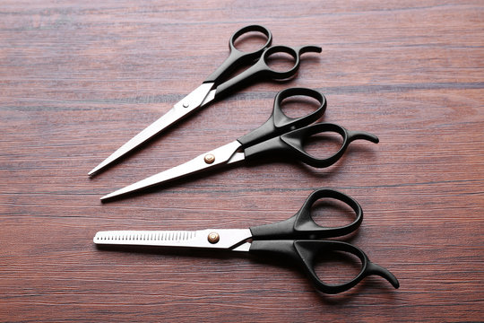 Three professional metal scissors with black handles lying on the wooden table, close up