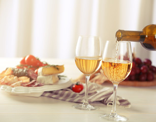 Pouring white wine into glass and food on table indoors