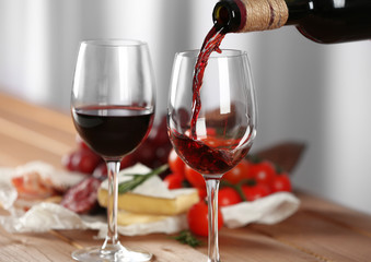 Pouring of red wine into glass and food on wooden table closeup