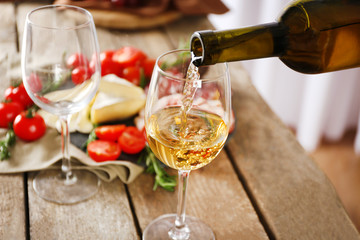 Pouring wine into glass and food on wooden table closeup