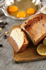 Composition of tasty cake with broken eggs and lemon on grey wooden background