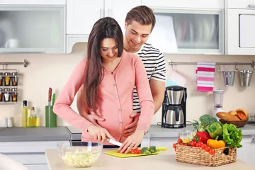 Papier Peint photo Cuisinier Pregnant woman with husband cooking food in kitchen