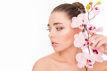 Fototapeta premium Beautiful young woman holding branch of orchid near her face