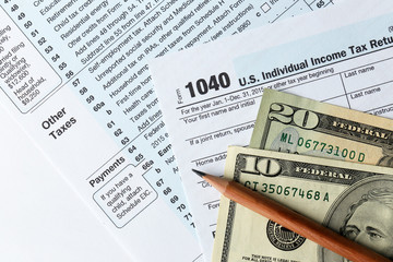 Obraz premium 1040 Individual Income Tax Return Form for 2015 year with a pencil to fill in and dollar bills on the white desk, close up