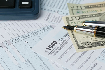 1040 Individual Income Tax Return Form for 2015 year with a pen to fill in and dollar bills, close up