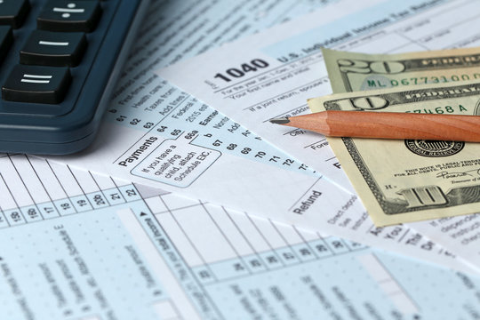 1040 Individual Income Tax Return Form for 2015 year with a pencil to fill in, calculator and dollar bills, close up