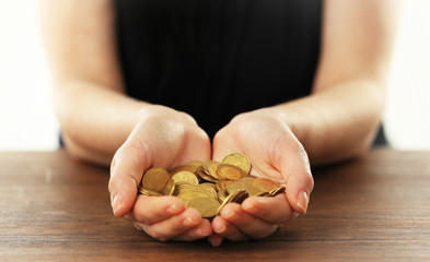 Young woman in a black shirt holding a heap of  coins in her hands above brown wooden table, close up