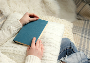 Obraz premium Young woman sitting on the sofa and holding a light-blue book cover on a white cushion, close up
