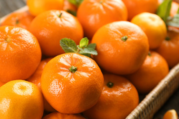 Wicker basket of delicious tangerines  with a  mint on the wooden table, close up