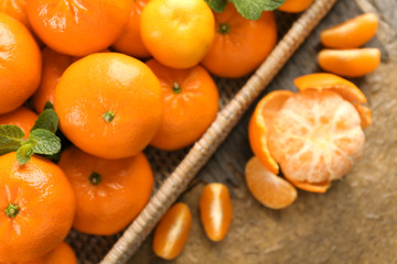 Delicious peeled tangerine beside  wicker basket of mandarins on the rustic table, top view