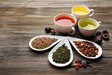 Tea concept. Different kinds of dry tea in ceramic bowls and cups of aromatic tea on wooden background