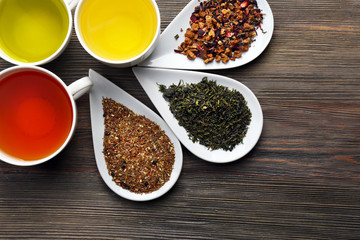 Tea concept. Different kinds of dry tea in ceramic bowls and cups of aromatic tea on wooden background
